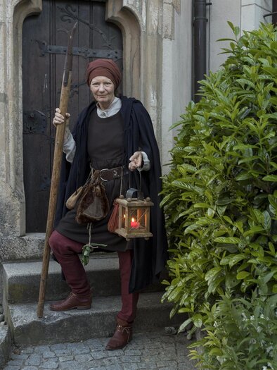 Ein mittelalterlicher Mann steht vor einer Tür und hält eine Laterne in der Hand. Er trägt traditionelle Kleidung und hat einen Gehstock dabei. | © Martin Meieregger