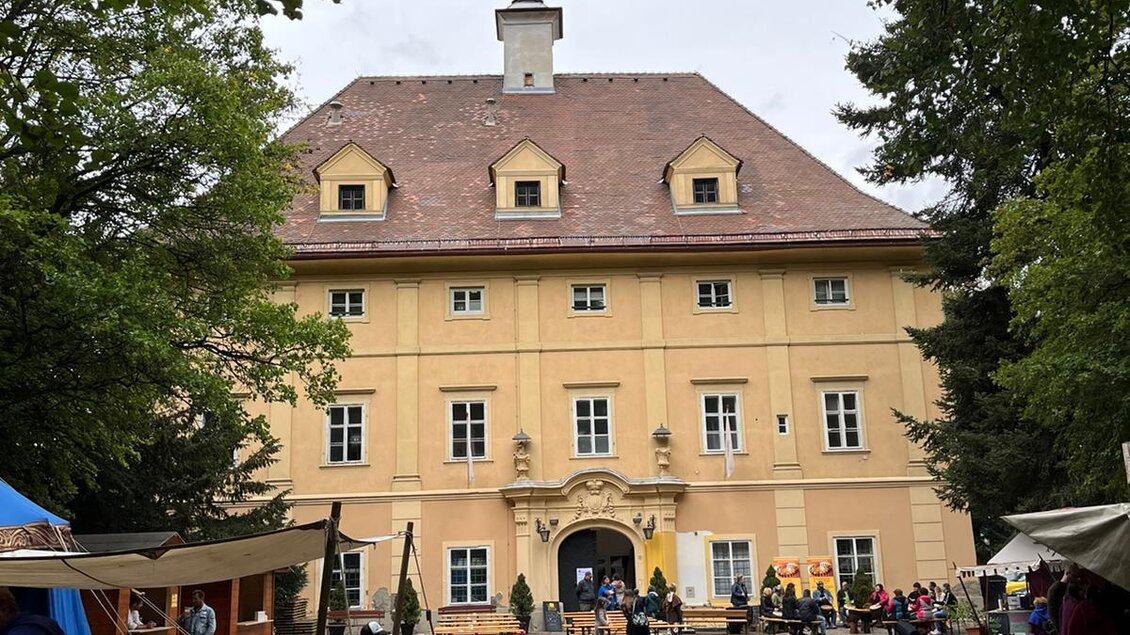 Ein historisches Gebäude umgeben von Bäumen. Im Vordergrund sind Zelte und Menschen versammelt. | © Erlebnisregion Murtal