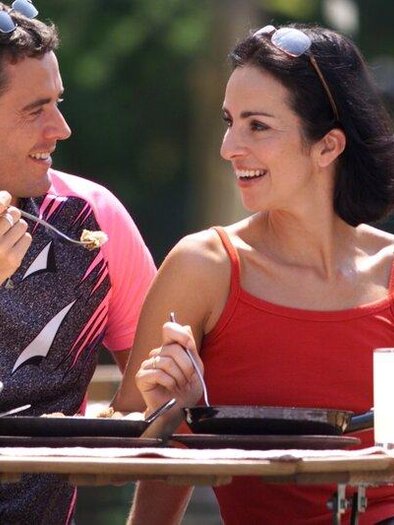 A laughing couple is sitting at a wooden table outdoors and enjoying a meal together. | © Kurkomission Bad Blumau