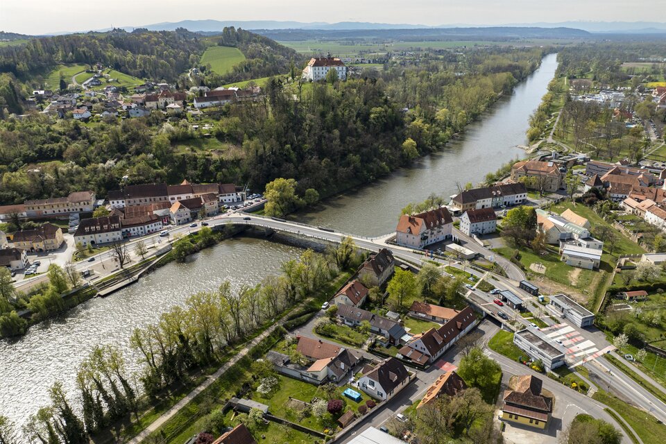 Eine malerische Landschaft mit einem Fluss, der durch eine kleine Stadt fließt. Umgeben von grünen Hügeln und Wohnhäusern. | © JueMa-Media