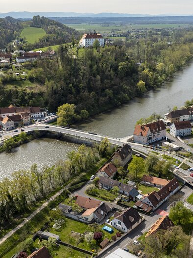 Eine malerische Landschaft mit einem Fluss, der durch eine kleine Stadt fließt. Umgeben von grünen Hügeln und Wohnhäusern. | © JueMa-Media