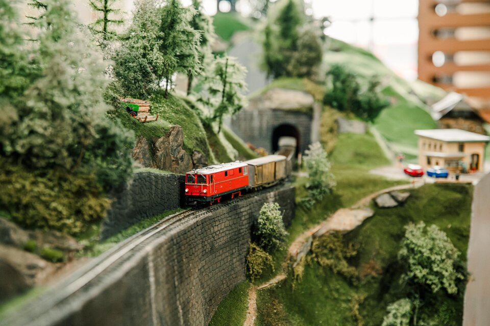 Modeleisenbahn mit Landschaft auf einen Viadukt fährt eine Zuggarnitur mit roter Lokomotive.  | © Region Graz-Mias Photoart