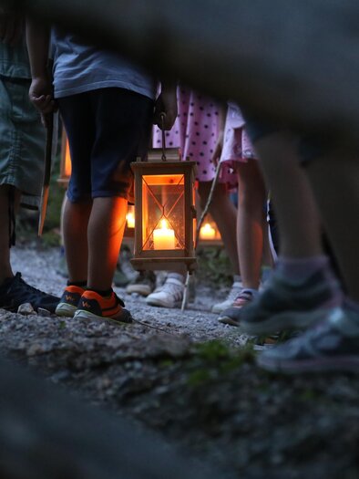 A group of children stands on a narrow path holding a lantern with a flaming light. In the background, more illuminated lanterns are visible. | © ÖFM-Christiane Becker
