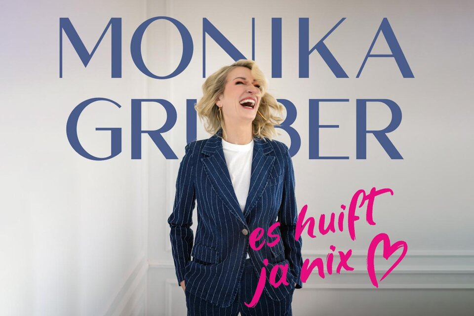 Eine lachende Frau in einem gestreiften Anzug steht vor einem neutralen Hintergrund. Der Text "MONIKA GRUBER" und "es huift ja nix" sind prominent im Bild platziert. | © (c)Starupphoto