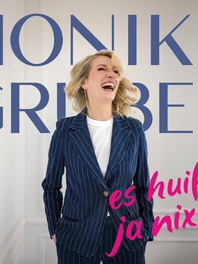 A laughing woman in a striped suit stands in front of a neutral background. The text "MONIKA GRUBER" and "it doesn't help at all" are prominently placed in the image. | © (c)Starupphoto