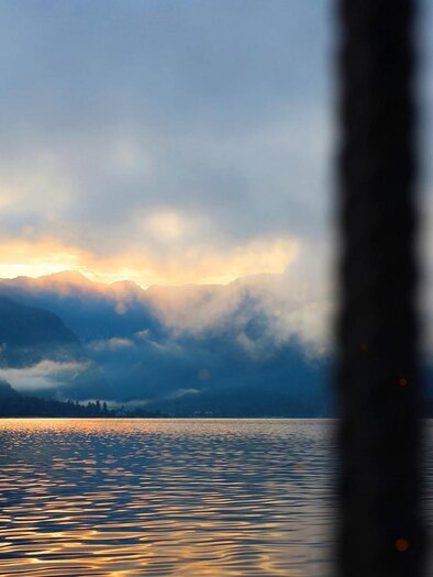 A tranquil seascape with mist and mountains in the background. The sky glows softly at sunrise. | © Schifffahrt Grundlsee Toplitzsee
