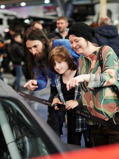 A family is curiously looking at a car at an exhibition. They are pointing at the vehicle with their finger and seem excited. | © Valerie_Maltseva