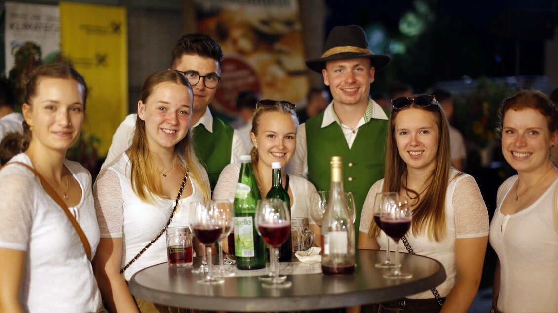 Eine Gruppe von fröhlichen Menschen steht um einen Tisch mit Getränken. Sie tragen traditionelle Trachten und lächeln in die Kamera. | © Oststeiermark Tourismus