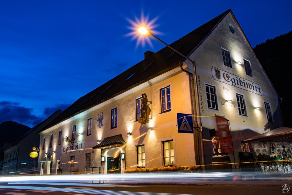 Ein historisches Gebäude in der Dämmerung, beleuchtet von Straßenlaternen. Die Fassade zeigt kunstvolle Verzierungen und Atmosphäre. | © Tv Murau