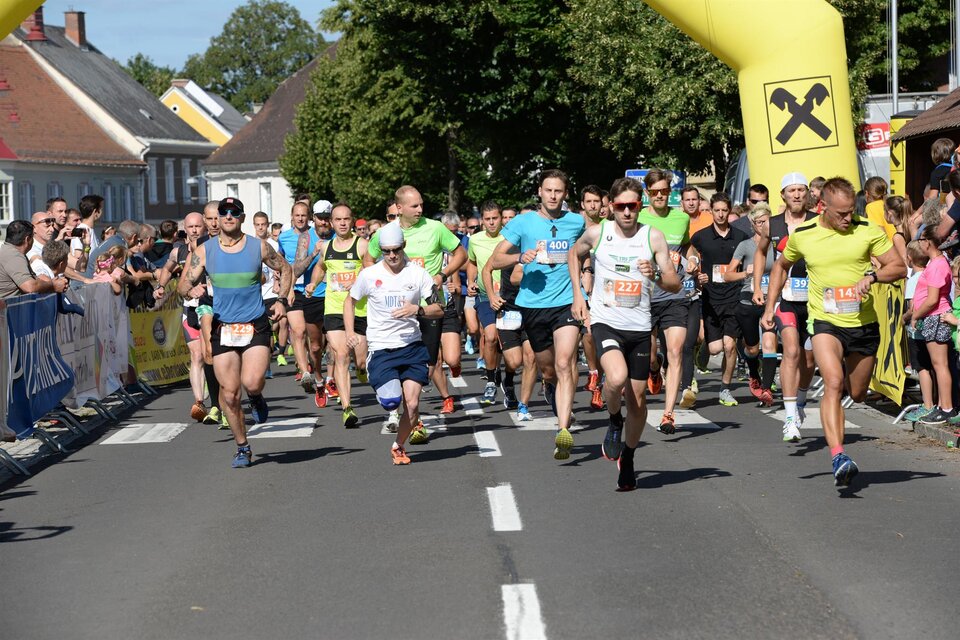 Eine Gruppe von Läufern startet ein Rennen auf einer belebten Straße. Im Hintergrund sind Zuschauer und grüne Bäume zu sehen. | © Foto de Monte