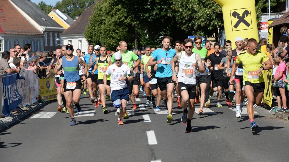 Eine Gruppe von Läufern startet ein Rennen auf einer belebten Straße. Im Hintergrund sind Zuschauer und grüne Bäume zu sehen. | © Foto de Monte