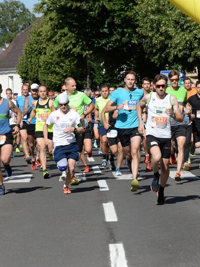 Eine Gruppe von Läufern startet ein Rennen auf einer belebten Straße. Im Hintergrund sind Zuschauer und grüne Bäume zu sehen. | © Foto de Monte