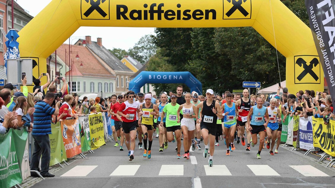 Eine Laufveranstaltung mit vielen Teilnehmern beim Start unter einem großen, gelben Bogen. Zuschauer stehen an der Strecke und unterstützen die Läufer. | © Murecker Aulauf