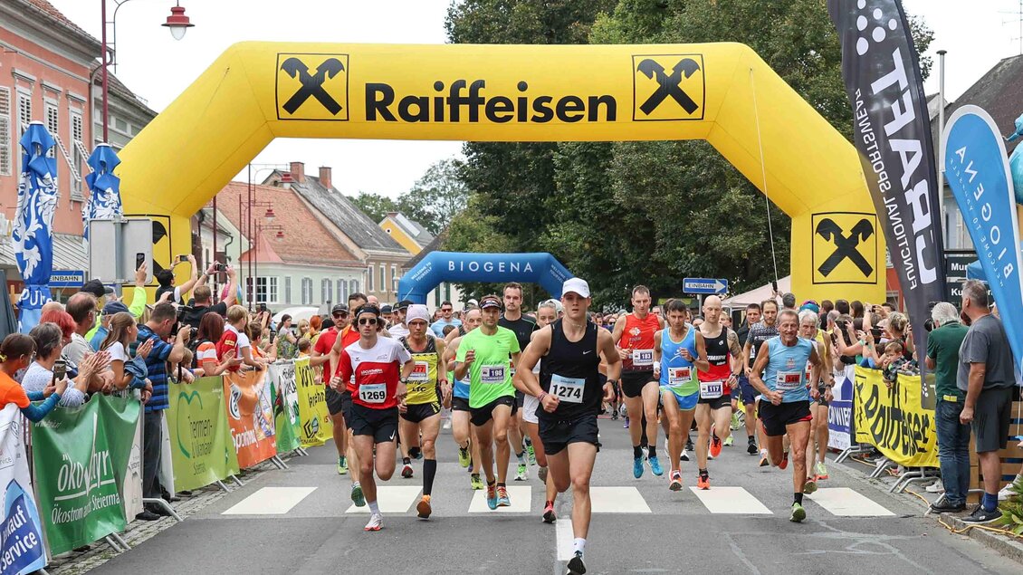 Ein Straßenlauf mit vielen Teilnehmern unter einem großen Bogen mit dem Logo von Raiffeisen. Die Atmosphäre ist festlich und es gibt zahlreiche Zuschauer am Rand. | © Murecker Aulauf