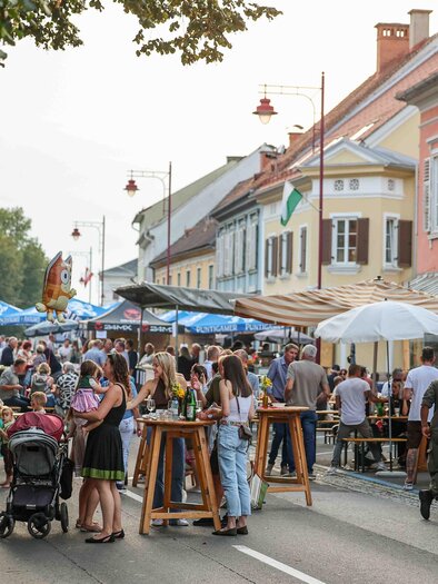 Eine belebte Straße mit vielen Menschen, die an Ständen sitzen und essen. Bunte Sonnenschirme und historische Gebäude umrahmen die Szene. | © Foto de Monte