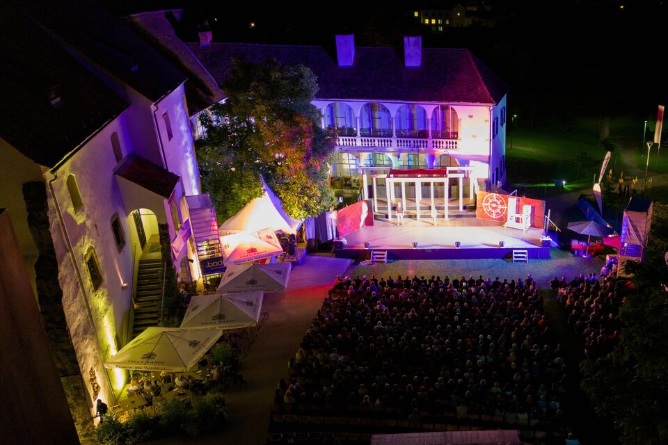 Eine beleuchtete Bühne bei Nacht vor einem historischen Gebäude. Das Publikum sitzt auf Stühlen und genießt die Veranstaltung. | © Oststeiermark Tourismus