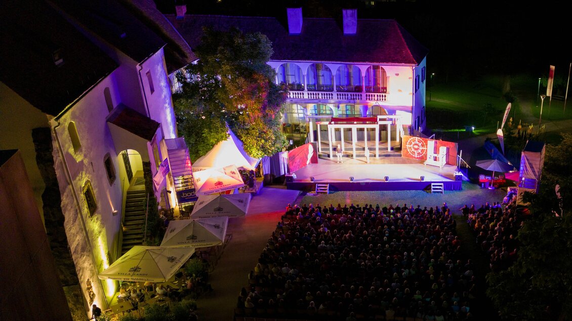 Eine beleuchtete Bühne bei Nacht vor einem historischen Gebäude. Das Publikum sitzt auf Stühlen und genießt die Veranstaltung. | © Oststeiermark Tourismus