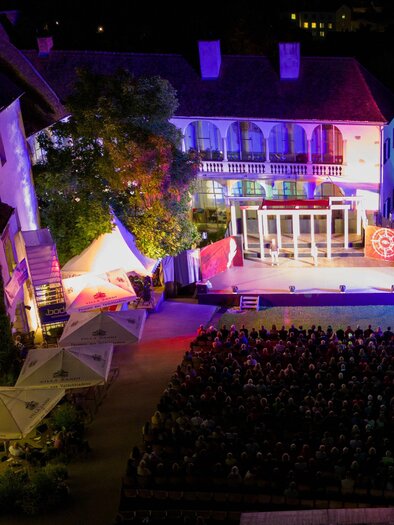 Eine beleuchtete Bühne bei Nacht vor einem historischen Gebäude. Das Publikum sitzt auf Stühlen und genießt die Veranstaltung. | © Oststeiermark Tourismus