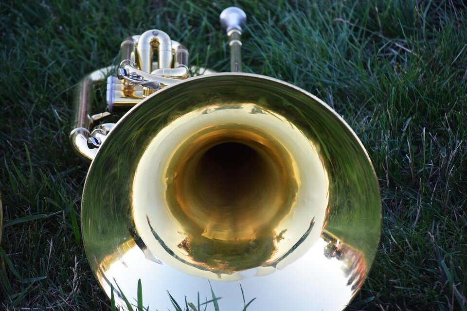 Eine große, glänzende Trompete liegt auf grünem Gras. Der Blick ins Innere des Instruments zeigt die reflektierende Oberfläche. | © Pixabay
