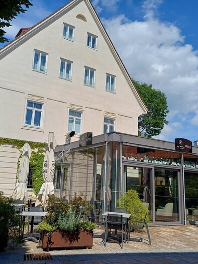 Ein charmantes Café mit einer großen Glasfassade und Außensitzplätzen. Umgeben von Bäumen und einem klaren blauen Himmel. | © TV Südsteiermark - Löschnig Irene