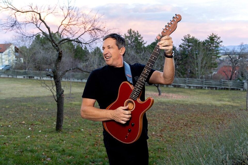 Ein Mann spielt eine Gitarre in einem Garten. Der Hintergrund zeigt Bäume und einen leicht bewölkten Himmel. | © Feelimage