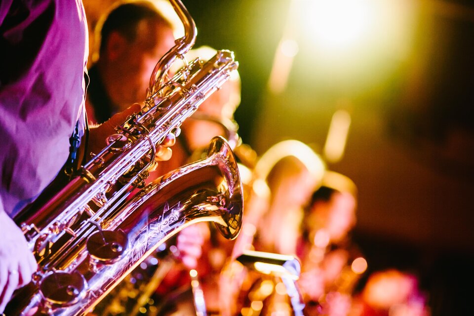 Eine Jazzband spielt auf der Bühne. Verschiedene Saxophone glitzern im Licht der Scheinwerfer.
