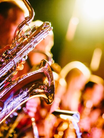 Eine Jazzband spielt auf der Bühne. Verschiedene Saxophone glitzern im Licht der Scheinwerfer.