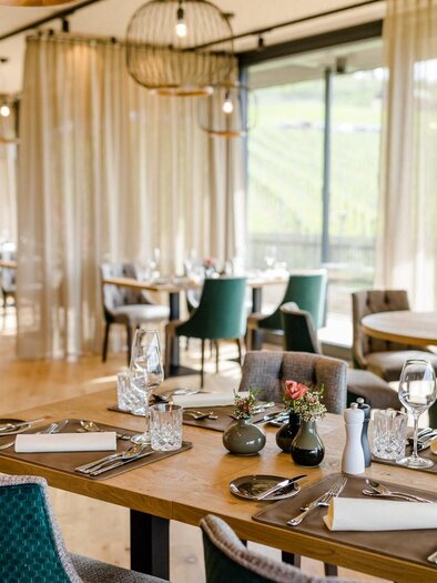 An elegant restaurant with wooden floors and modern furniture. Tables are neatly set, and large windows offer a view of the surrounding landscape. | © Karin Bergmann
