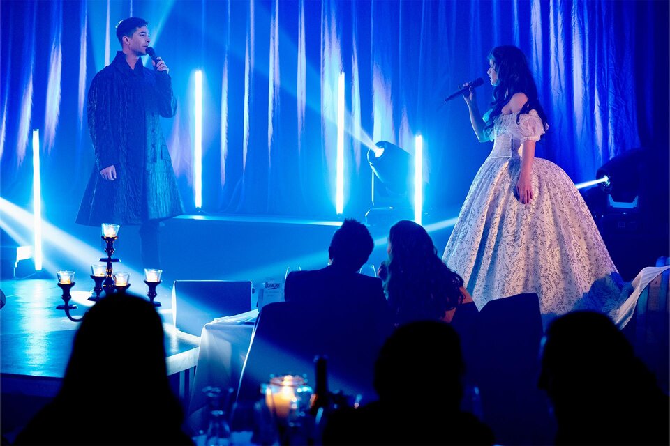 Ein musikalisches Duett auf einer Bühne. Zwei Sänger stehen in stilvollen Outfits vor beleuchtetem Hintergrund und performen für ein Publikum. | © Anja Wendzel