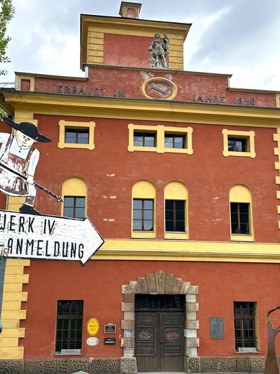 Ein rotes historisches Gebäude mit grünen Bäumen im Vordergrund. Ein Schild weist auf Führungen hin. | © TVB Erzberg-Leoben