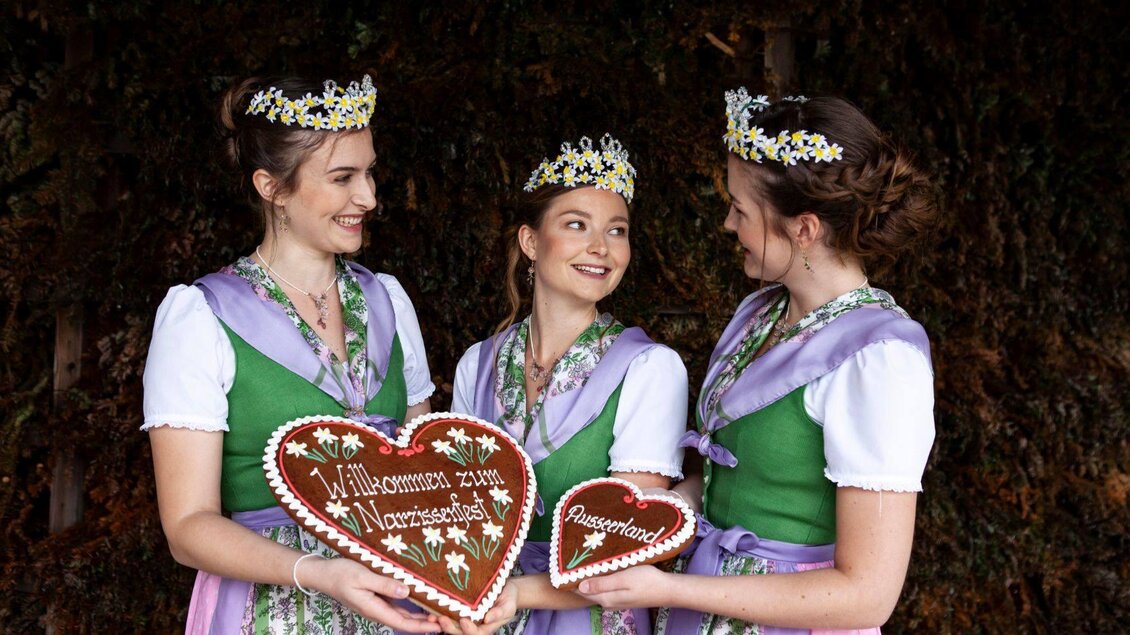 Die drei Narzissenhoheiten in traditionellen Trachten halten große Lebkuchenherzen von der Ausseer Lebzelterei.  | © SIMA