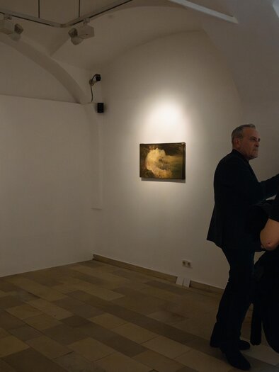 Eine Kunstgalerie mit zwei Bildern an der Wand. Personen stehen zusammen und betrachten die Kunstwerke. | © Achromatic Photography
