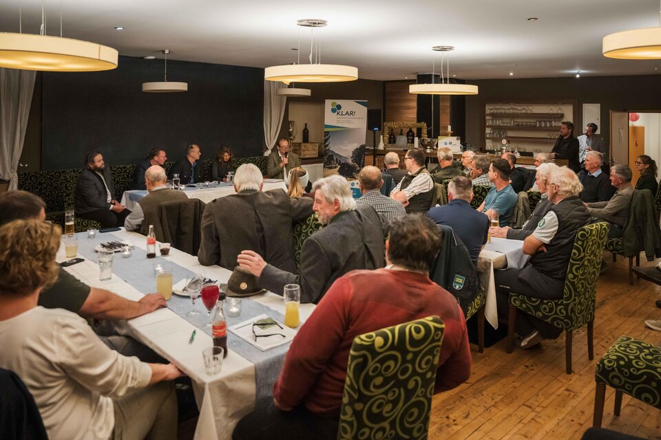 Eine Menschenmenge sitzt an einem großen Tisch in einem Restaurant. Im Vordergrund findet eine Diskussion statt, während die Teilnehmer aufmerksam zuhören. | © NUP Eisenwurzen