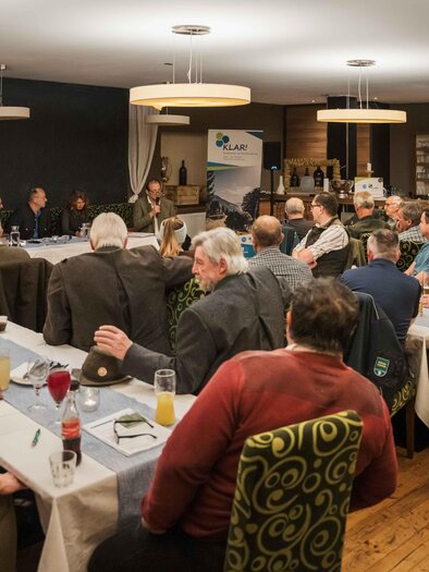 Eine Menschenmenge sitzt an einem großen Tisch in einem Restaurant. Im Vordergrund findet eine Diskussion statt, während die Teilnehmer aufmerksam zuhören. | © NUP Eisenwurzen