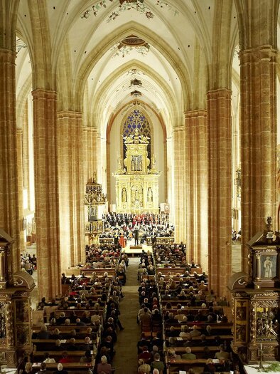 Eine große Kirche mit hohen, gewölbten Decken und kunstvollen Verzierungen. Die Bankreihen sind voll mit Menschen, die einer Aufführung oder Zeremonie folgen. | © Verein Neuberger Kulturtage
