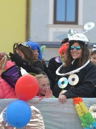 Eine fröhliche Parade mit bunten Kostümen und vielen Luftballons. Menschen lachen und feiern gemeinsam auf einem festlichen Wagen.