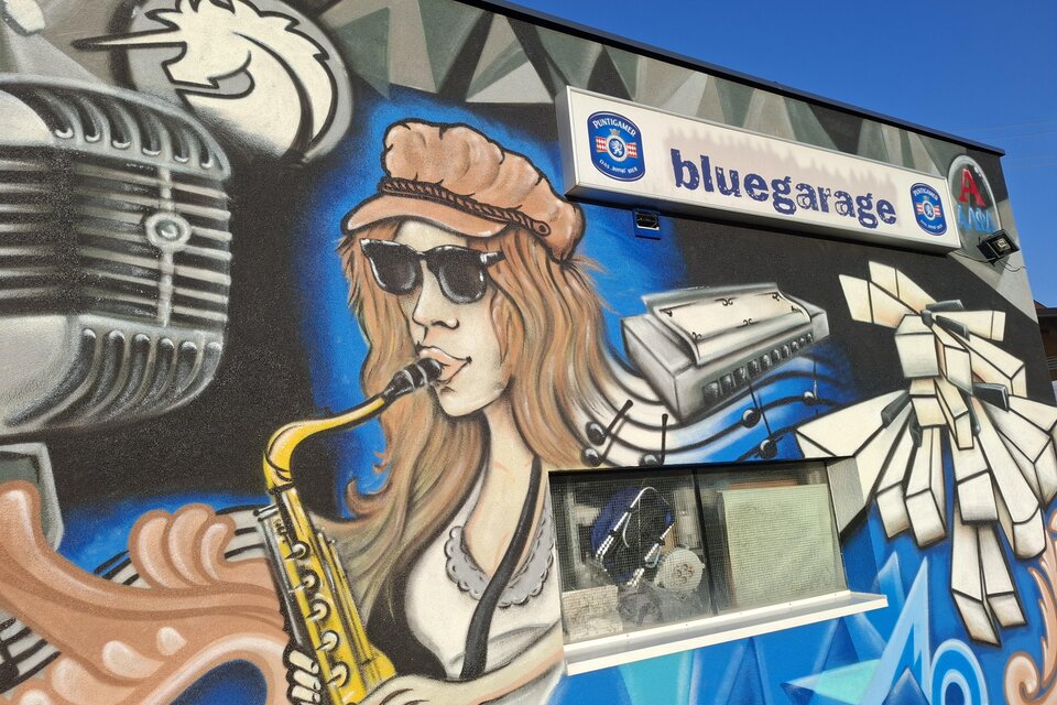 Eine bunte Wandmalerei mit einer Frau, die Saxophon spielt. Im Hintergrund sind musikalische Elemente und das Logo eines Unternehmens zu sehen. | © TVB_Steininger