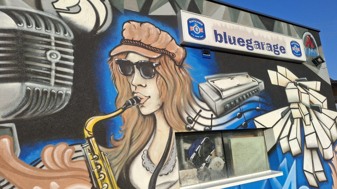 Eine bunte Wandmalerei mit einer Frau, die Saxophon spielt. Im Hintergrund sind musikalische Elemente und das Logo eines Unternehmens zu sehen. | © TVB_Steininger