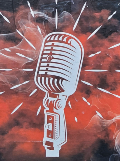 A stylized microphone in front of a red background with smoke clouds. The radiant lines around the microphone indicate energy and creativity. | © Kulturreferat Niklasdorf