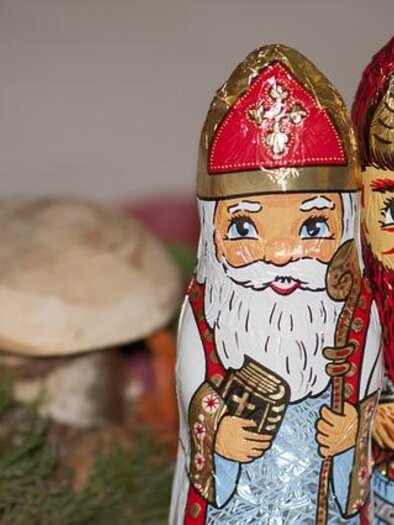 Two brightly painted figures representing a Santa Claus and a Christkind. In the background, natural elements like a small mushroom and green branches are visible. | © Pixabay