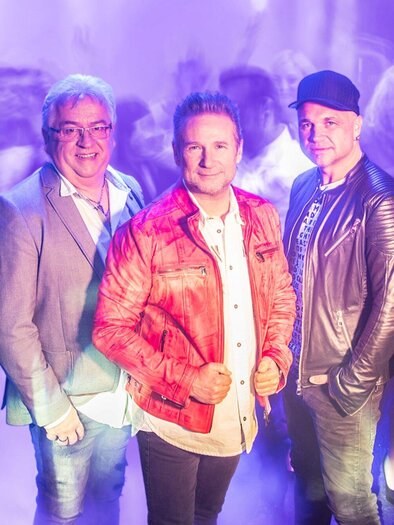 A group of five men stands in front of a blurred background. They pose in stylish outfits and seem to be having fun. | © Die Nockis