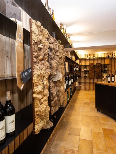 A stylish wine cellar with shelves full of wine bottles. In the center is a table, surrounded by warm wood paneling. | © Weinhof Scharl