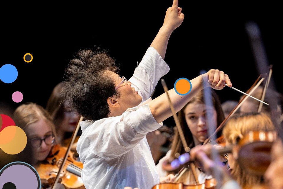 Ein Dirigent steht auf der Bühne und leitet ein Orchester. Im Hintergrund sind Musiker mit ihren Instrumenten zu sehen. | © Nikola Milatovic