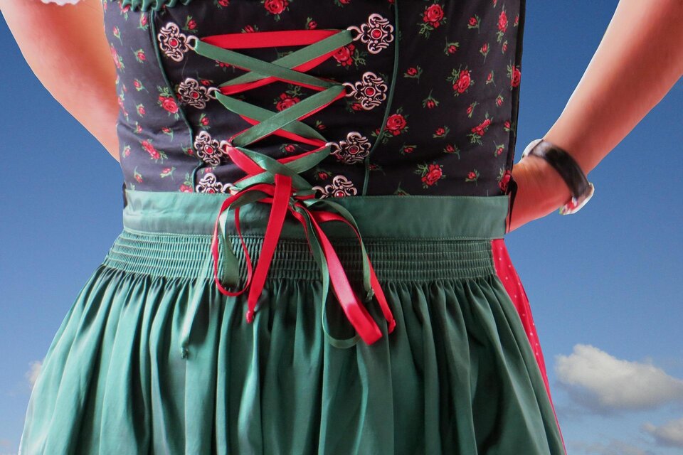 Eine Person trägt ein traditionelles Outfit mit einer rot-blauen Bluse und einem roten Rock. Die Hände sind mit dem Festbinden des Outfits beschäftigt. | © Pixabay