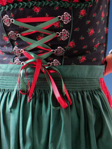 Eine Person trägt ein traditionelles Outfit mit einer rot-blauen Bluse und einem roten Rock. Die Hände sind mit dem Festbinden des Outfits beschäftigt. | © Pixabay
