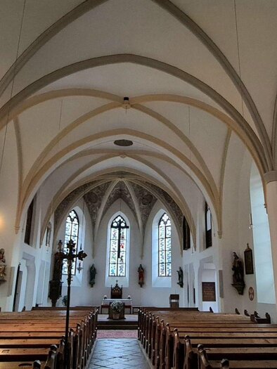 Eine künstlerische Innenansicht einer Kirche mit gewölbten Decken und alten Holzbänken. Die bunten Fenster lassen sanftes Licht in den Raum strömen. | © Stephanie Bor