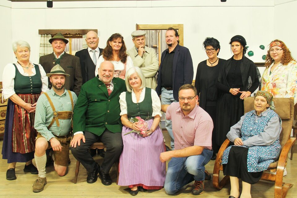 Eine Gruppe von Menschen in traditionellen Kleidungen pose für ein Foto. Sie stehen und sitzen in einem hellen Raum mit rustikalem Hintergrund. | © Obersteirische Volksbühne