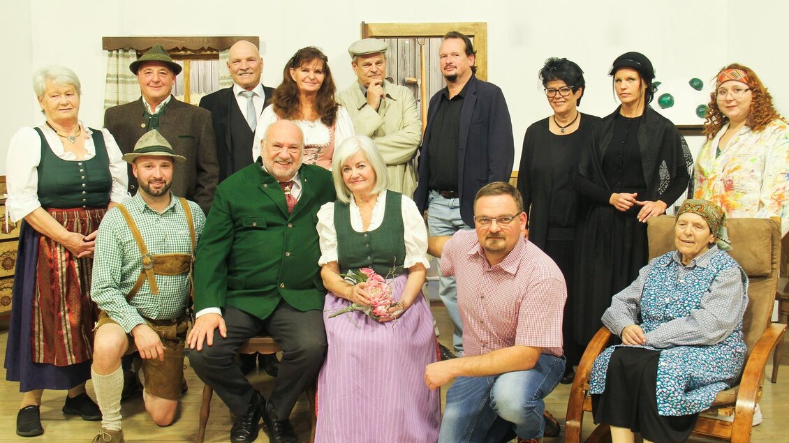 Eine Gruppe von Menschen in traditionellen Kleidungen pose für ein Foto. Sie stehen und sitzen in einem hellen Raum mit rustikalem Hintergrund. | © Obersteirische Volksbühne