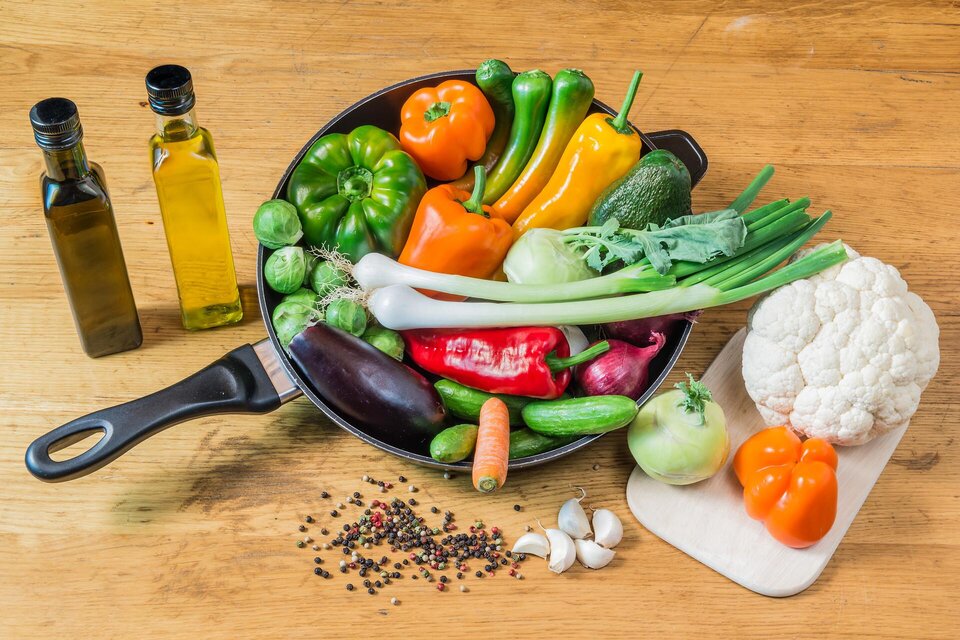 Eine Vielzahl frischer Gemüse ist in einer Pfanne arrangiert, darunter Paprika, Zucchini und Blumenkohl. Daneben befinden sich zwei Flaschen Olivenöl und verschiedene Gewürze. | © NP Gesäuse