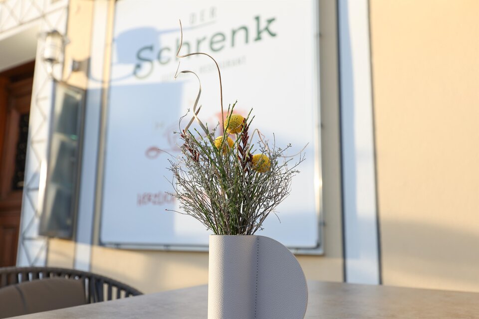 Eine dekorative Blumenvase mit getrockneten Blumen steht auf einem Tisch. Im Hintergrund ist ein Schild mit dem Namen "Schrenk" zu sehen. | © Tourismusverband Oststeiermark